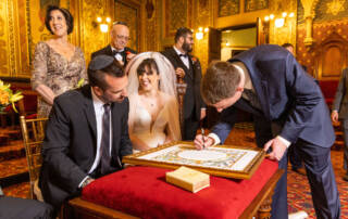 Bride and groom seated while man signs framed document