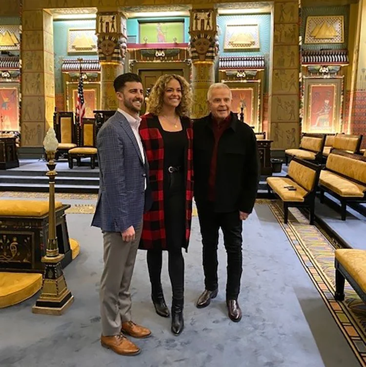 Smiling woman and two men standing together in Egyptian-styled lodge room.