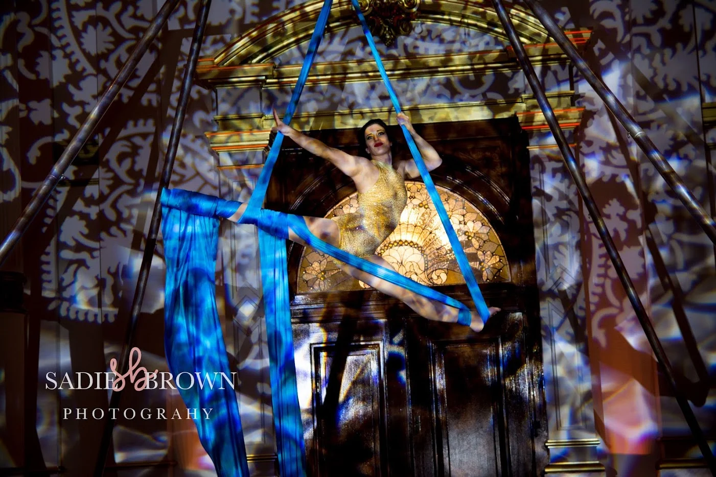 Corporate Aerialist in Ballroom 4 – Sadie&Brown Photography Woman in costume performing using ropes hanging from the ceiling with lighting pattern behind her