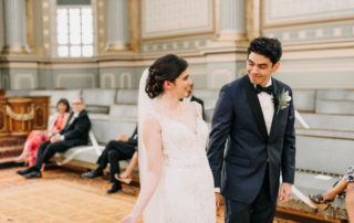Bride and groom smiling and holding hands as they walk in front of seated audience