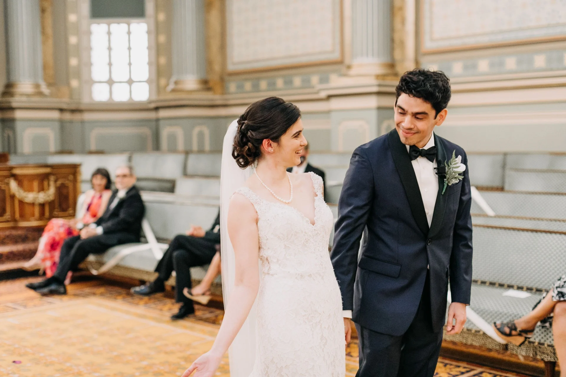 Bride and groom smiling and holding hands as they walk in front of seated audience
