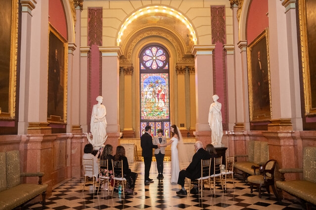 Couple getting married in foyer surrounded by group of five in chairs