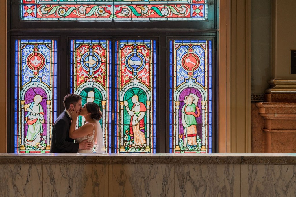 Bride and groom kissing with stained glass window behind them