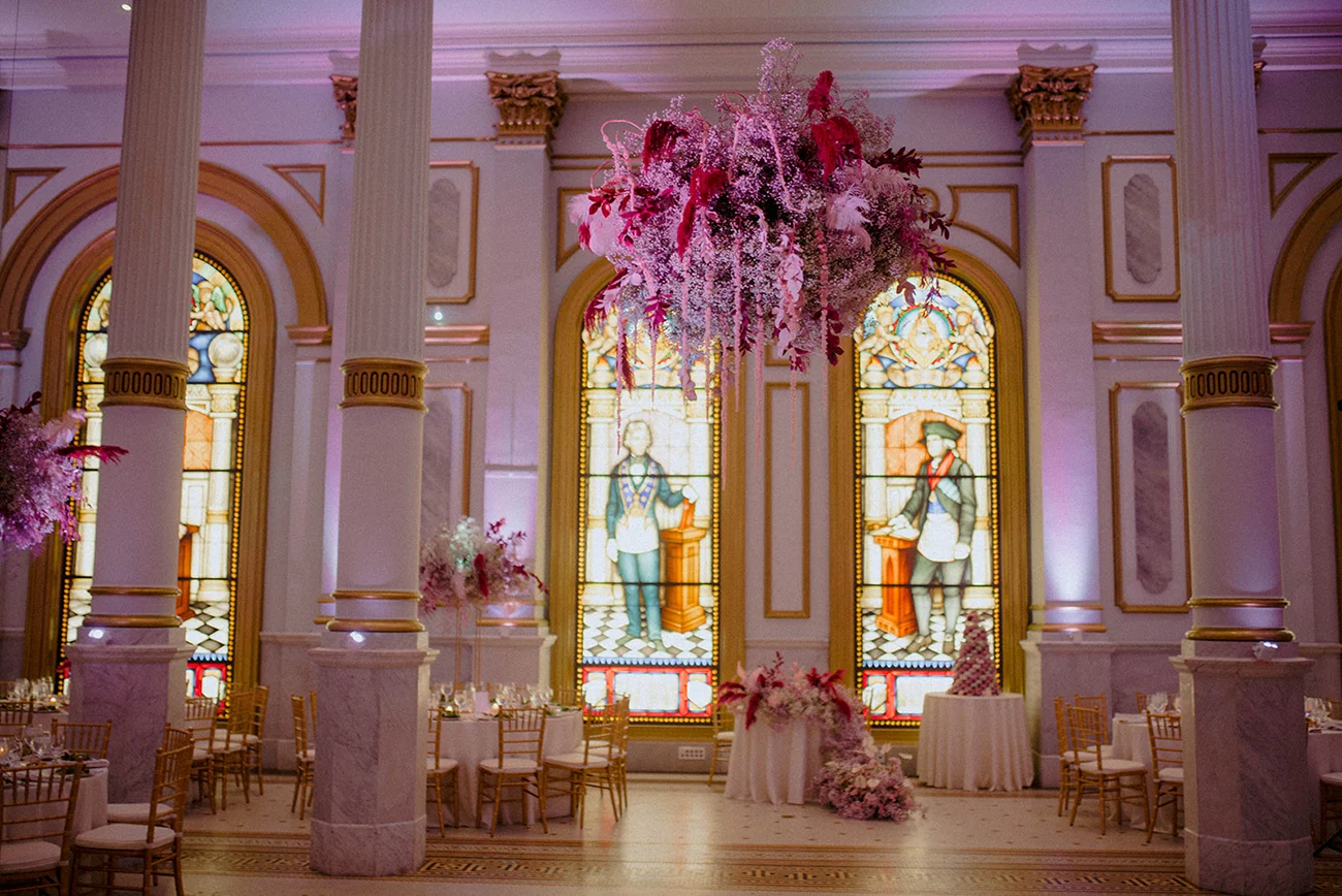 Casey & Trevor- Laura Huertas Photography-515 Stunning pink floral and feathered ceiling installations in large ballroom with glass windows and columns in the background.