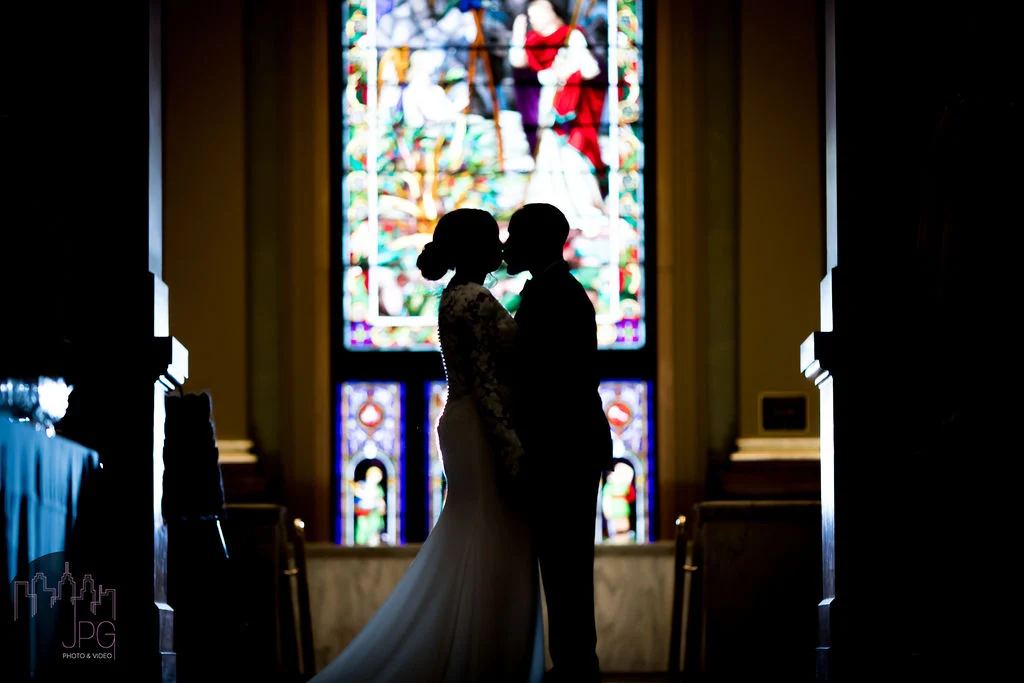 JPG Photography (2) Kissing bride and groom silhouetted in front of a stained glass window.