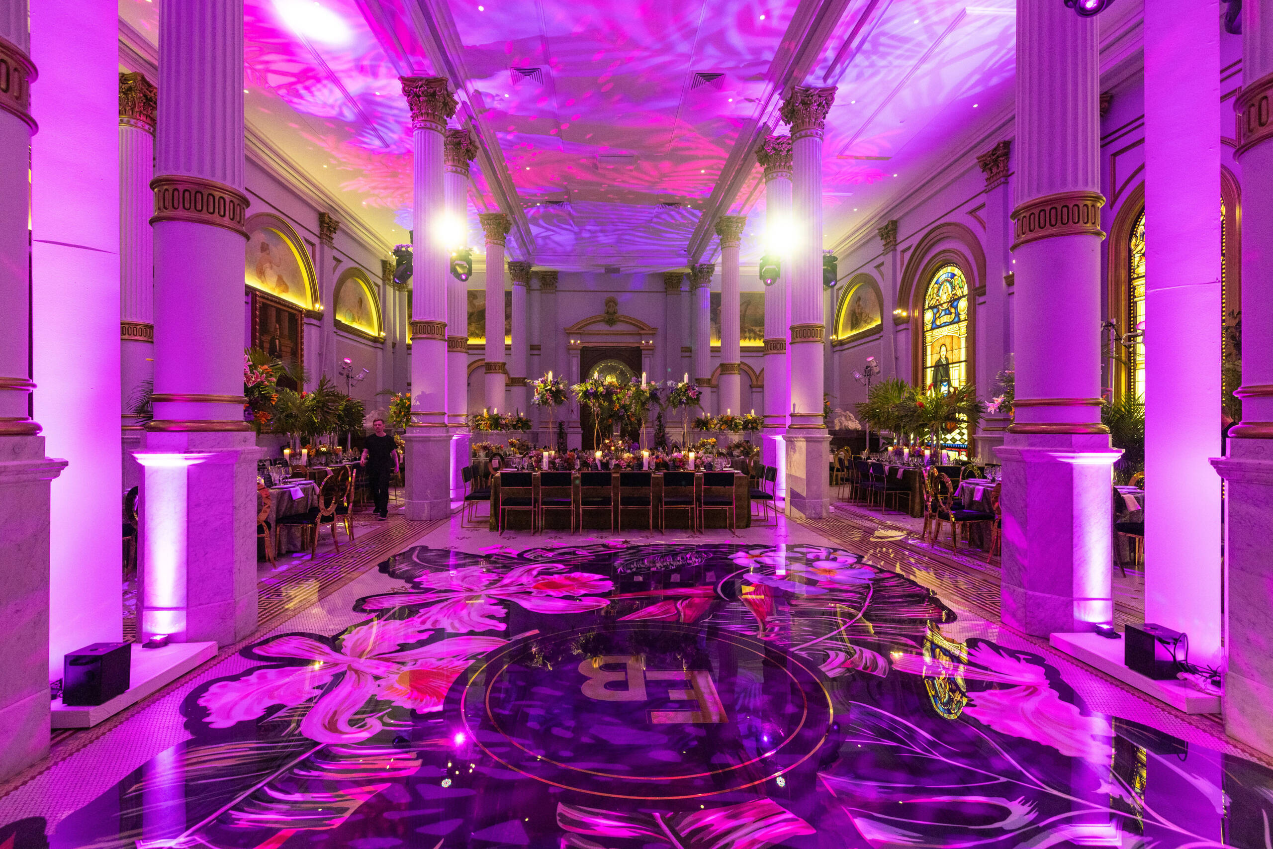 Purple-lit banquet hall with customized dance floor and tables in the background.