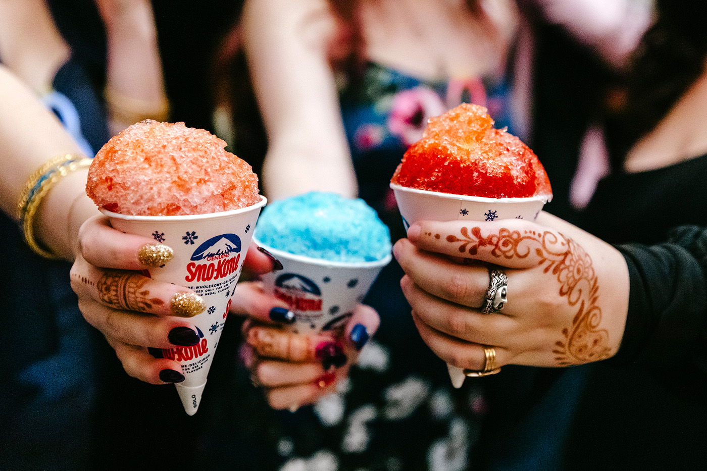 Close up of women's hands holding snow cone cups.