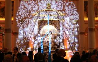 Acrobat artist performing on ribbons, highlighted by decorative lighting, in front of a crowd.