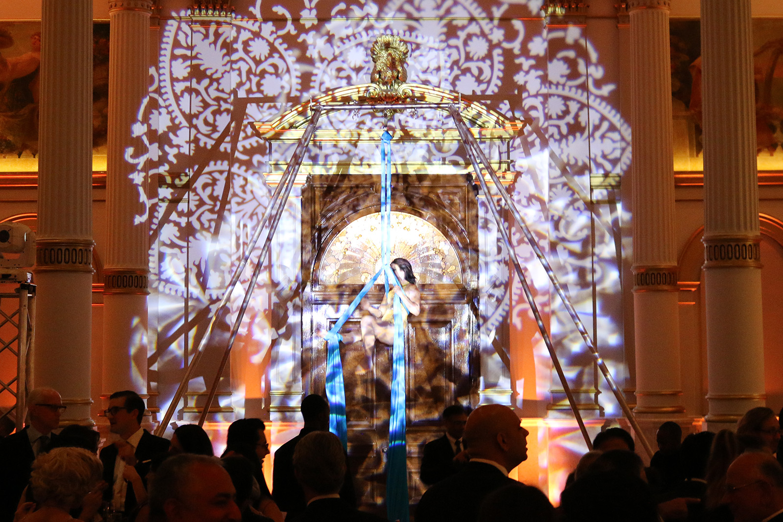 IMG_7768 (2) Acrobat artist performing on ribbons, highlighted by decorative lighting, in front of a crowd.