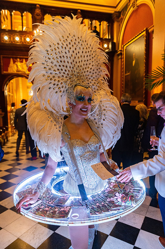 Jana Bannan Photography1 (1) Woman in feathered outfit and skirt with a round serving tray of snacks around her.