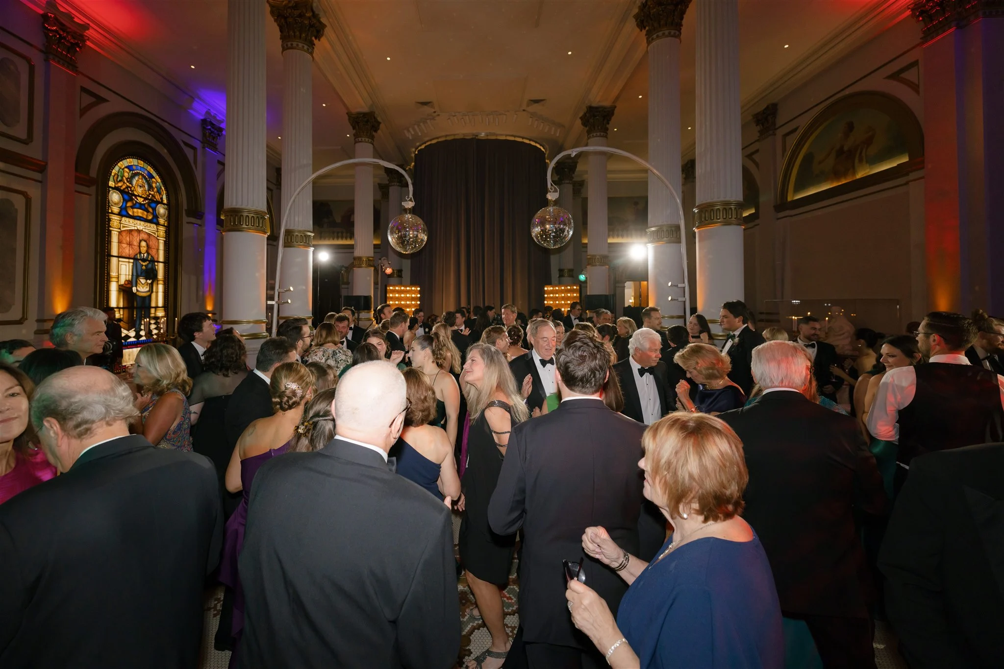 LAURA & MILES | WEDDING Group in formal attire dancing in a large ballroom. Two disco balls can be seen overhead.